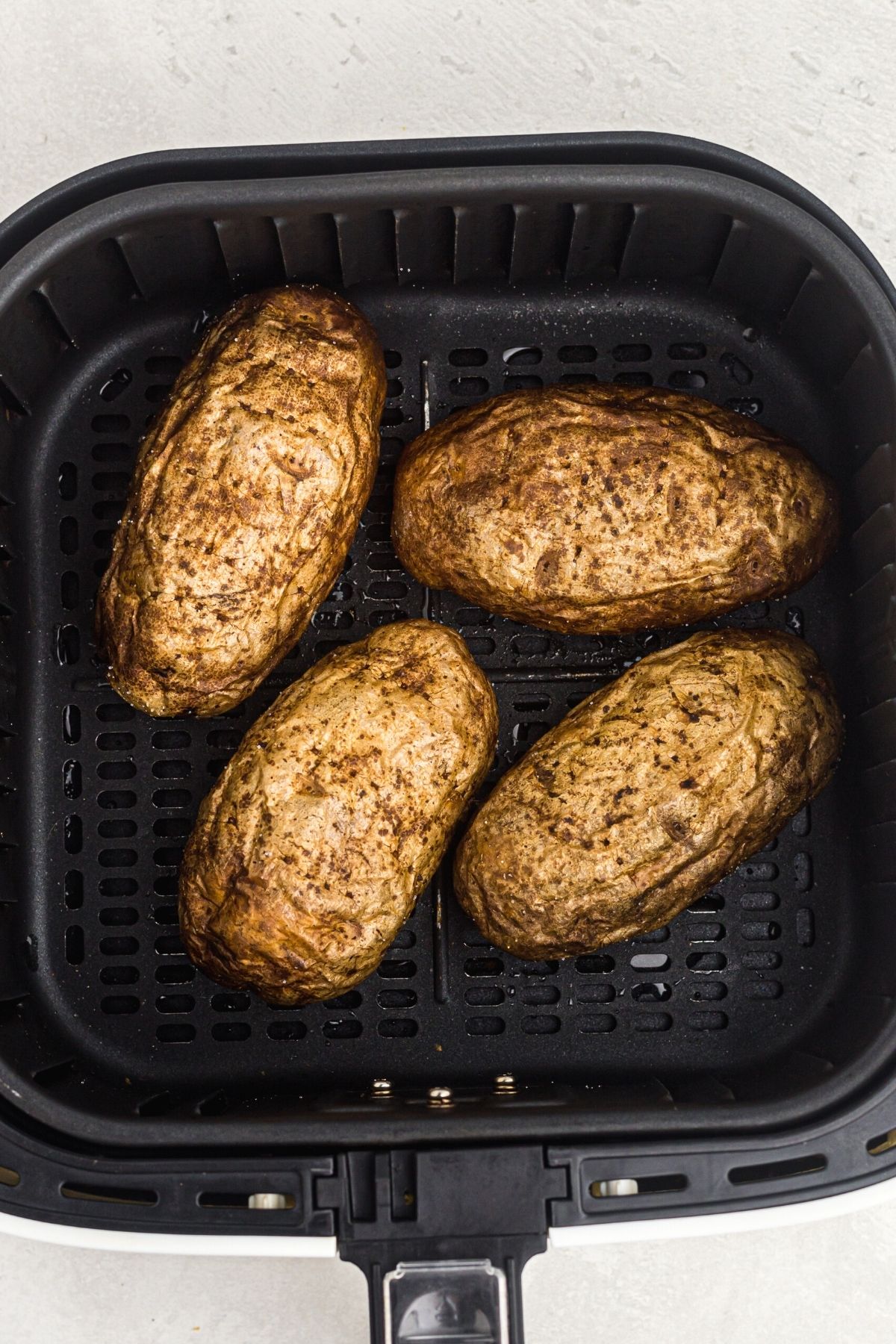 Four potatoes in the air fryer basket after being cooked.