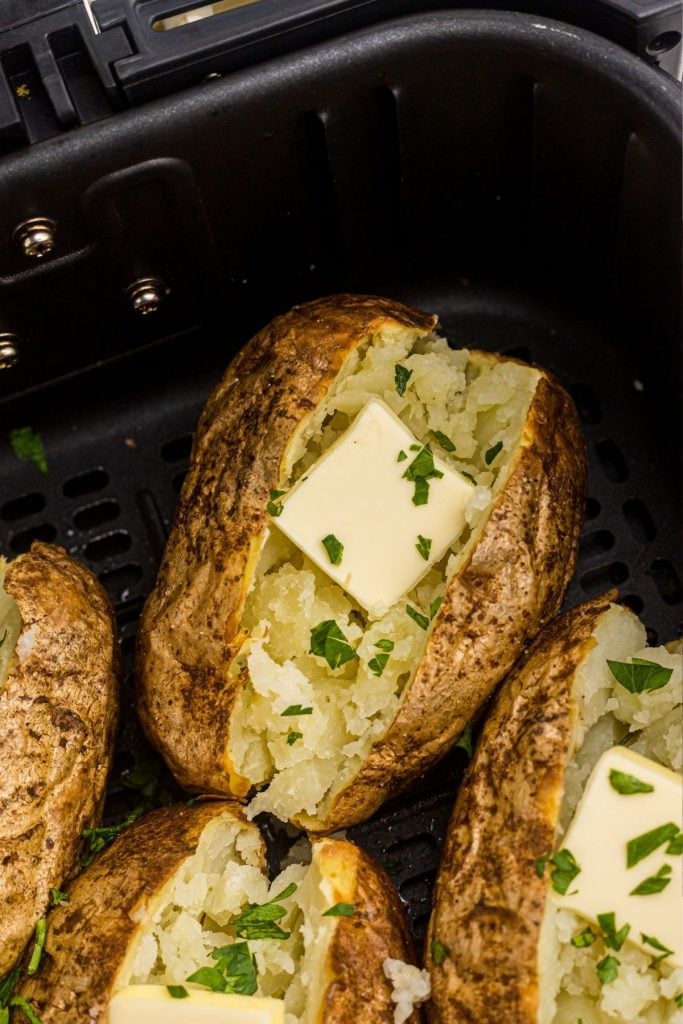 Golden brown potatoes topped with butter and parsley flakes, in the air fryer basket. 