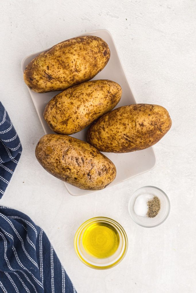 Ingredients to make baked potatoes, olive oil, salt and pepper on a white marble table. 