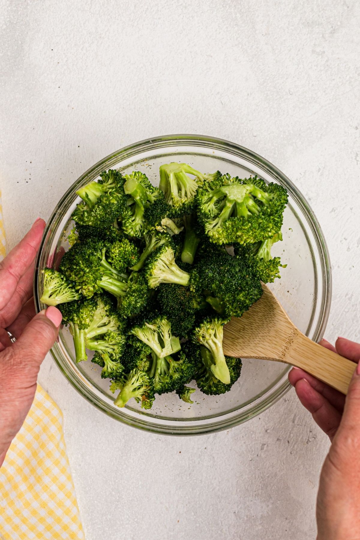 Glass bowl with broccoli and seasonings, being tossed with olive oil