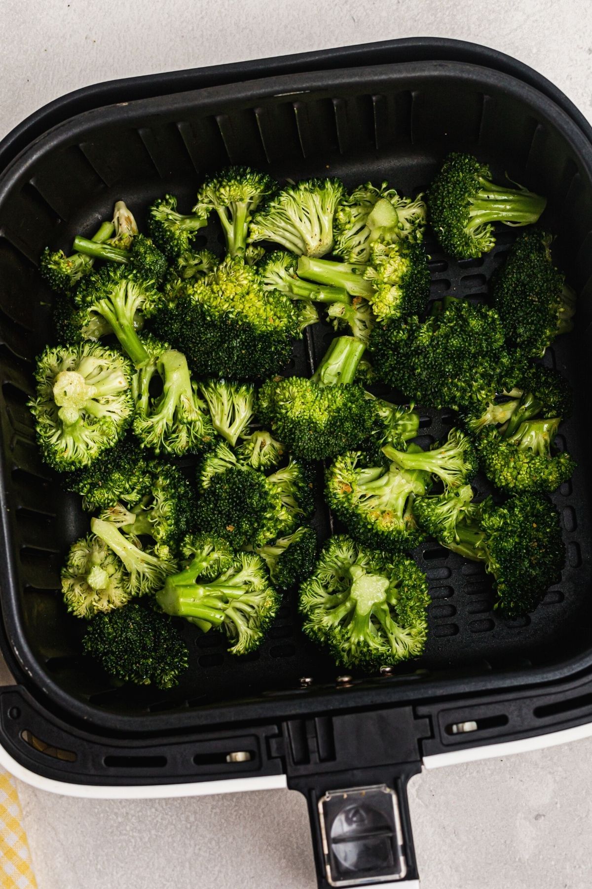 Uncooked seasoned broccoli florets in the air fryer basket