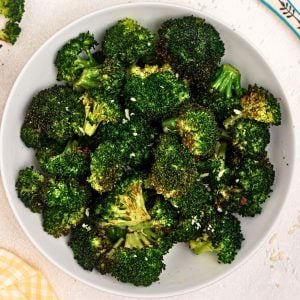Green cooked broccoli in a white bowl seasoned and sprinkled with parmesan cheese.