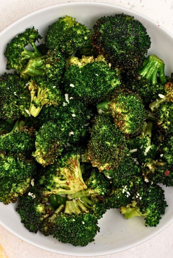 Green cooked broccoli in a white bowl seasoned and sprinkled with parmesan cheese.