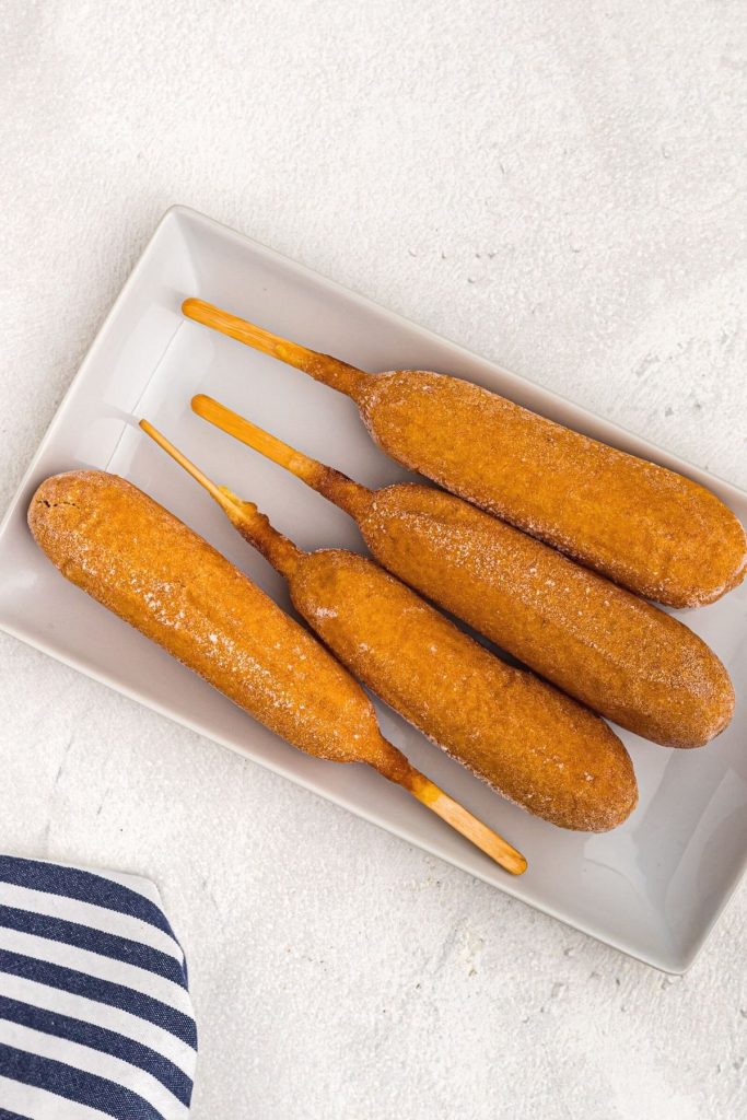 Frozen corn dogs on a white plate on a marble table before being cooked in the air fryer. 