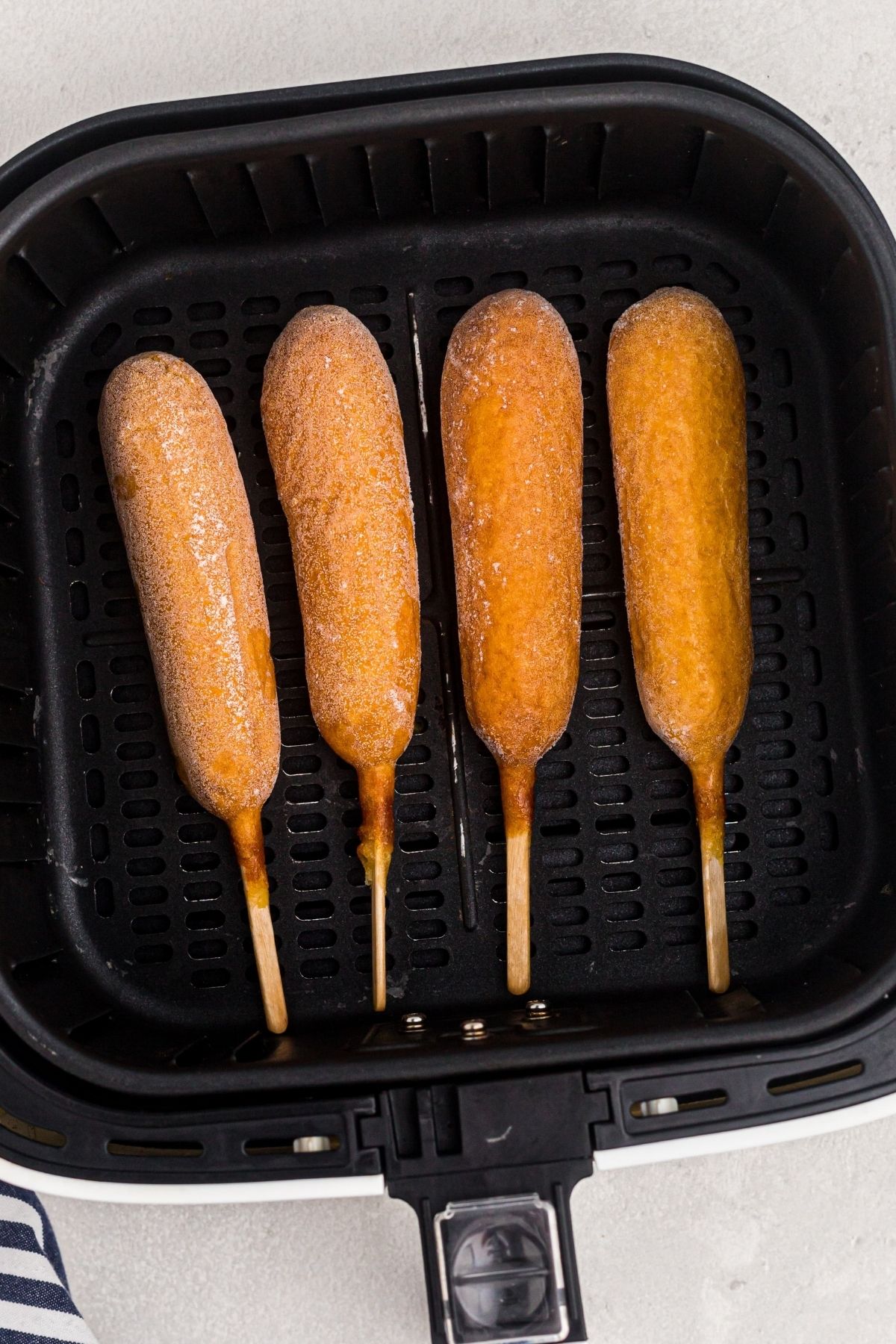 Four frozen corn dogs in an air fryer basket before being cooked