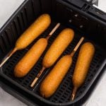 Golden corn dogs in the air fryer basket after being cooked