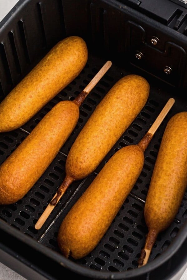 Golden corn dogs in the air fryer basket after being cooked