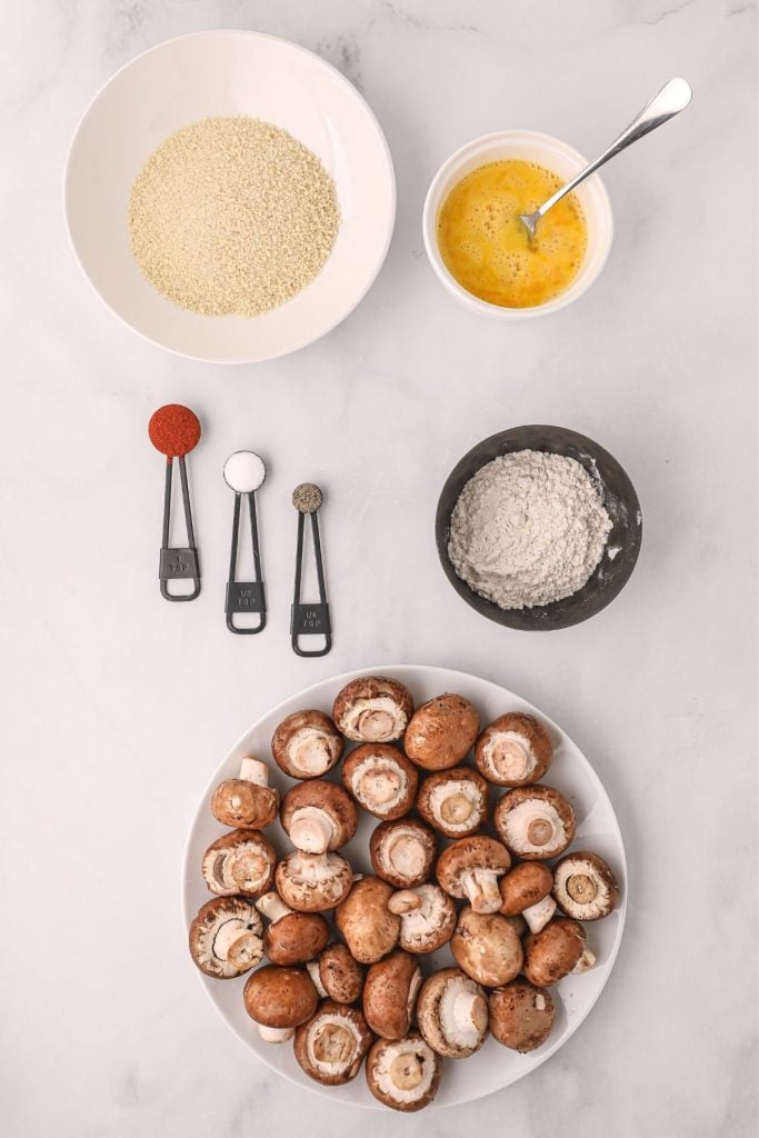 Ingredients needed to make fried mushrooms on a white table with mushrooms on a white plate