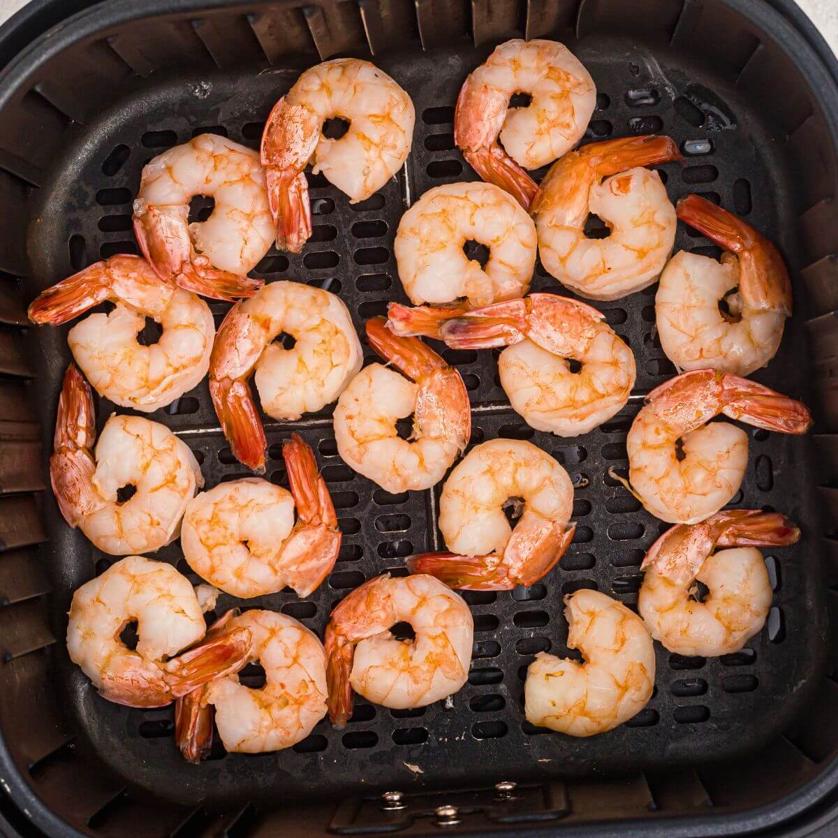 Juicy orange shrimp in the air fryer basket after being cooked from frozen.