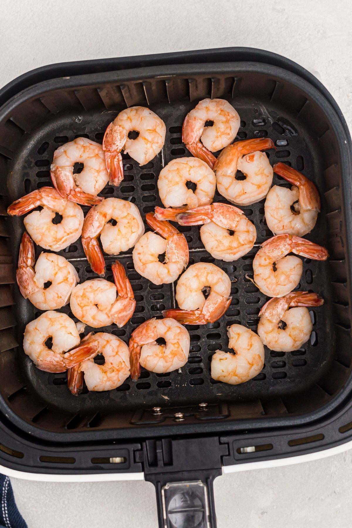 Orange frozen shrimp in the air fryer basket before being cooked