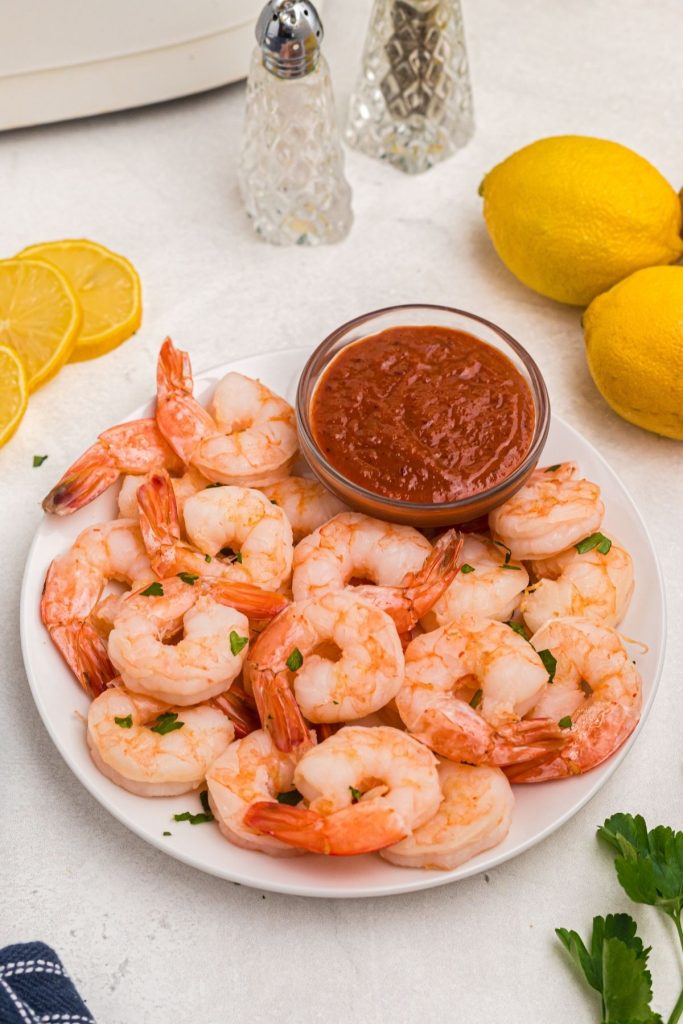 Juicy orange shrimp on a white plate with sliced lemons and salt and pepper on table.