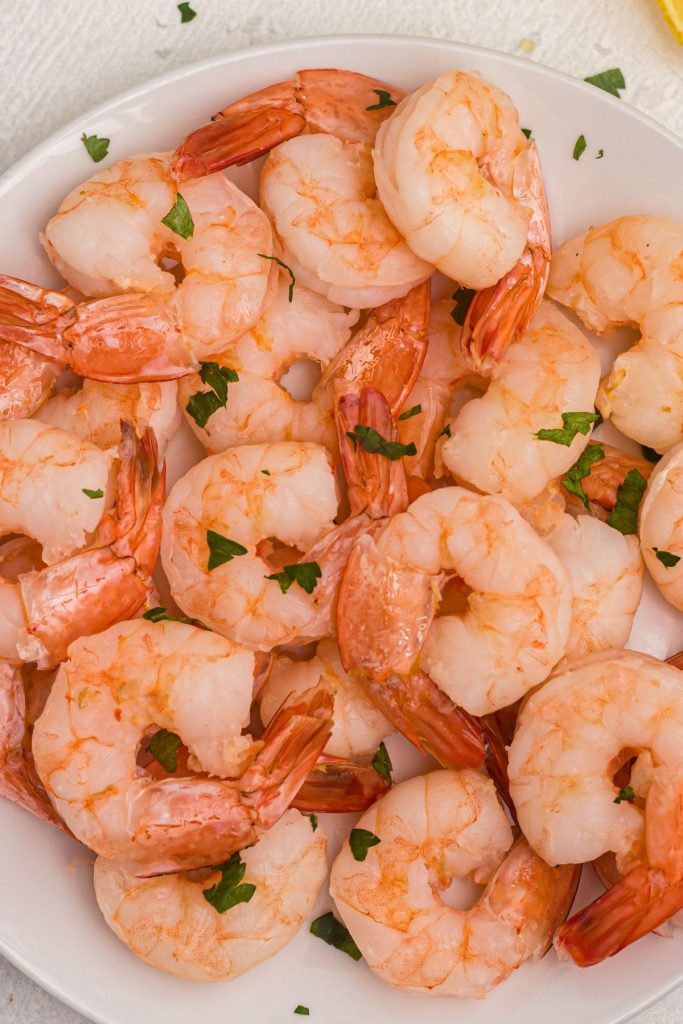 Orange juicy cooked shrimp on a white plate, garnished with parsley flakes