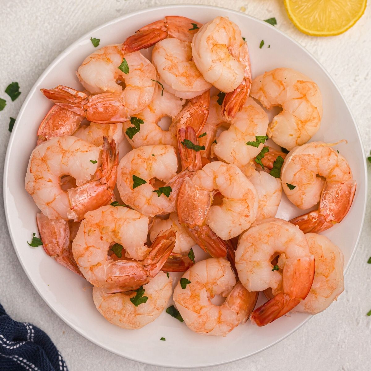 Juicy orange shrimp on a white plate, garnished with lemon slices and parsley flakes on a white plate.