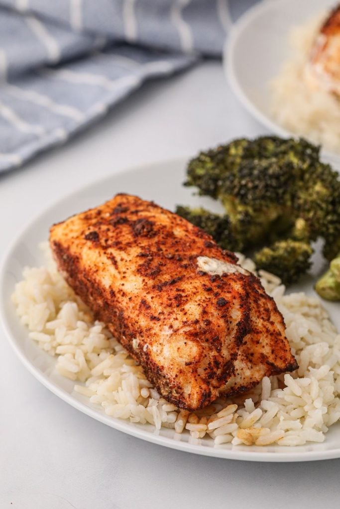 Juicy seasoned halibut filet on a white plate served with rice and broccoli