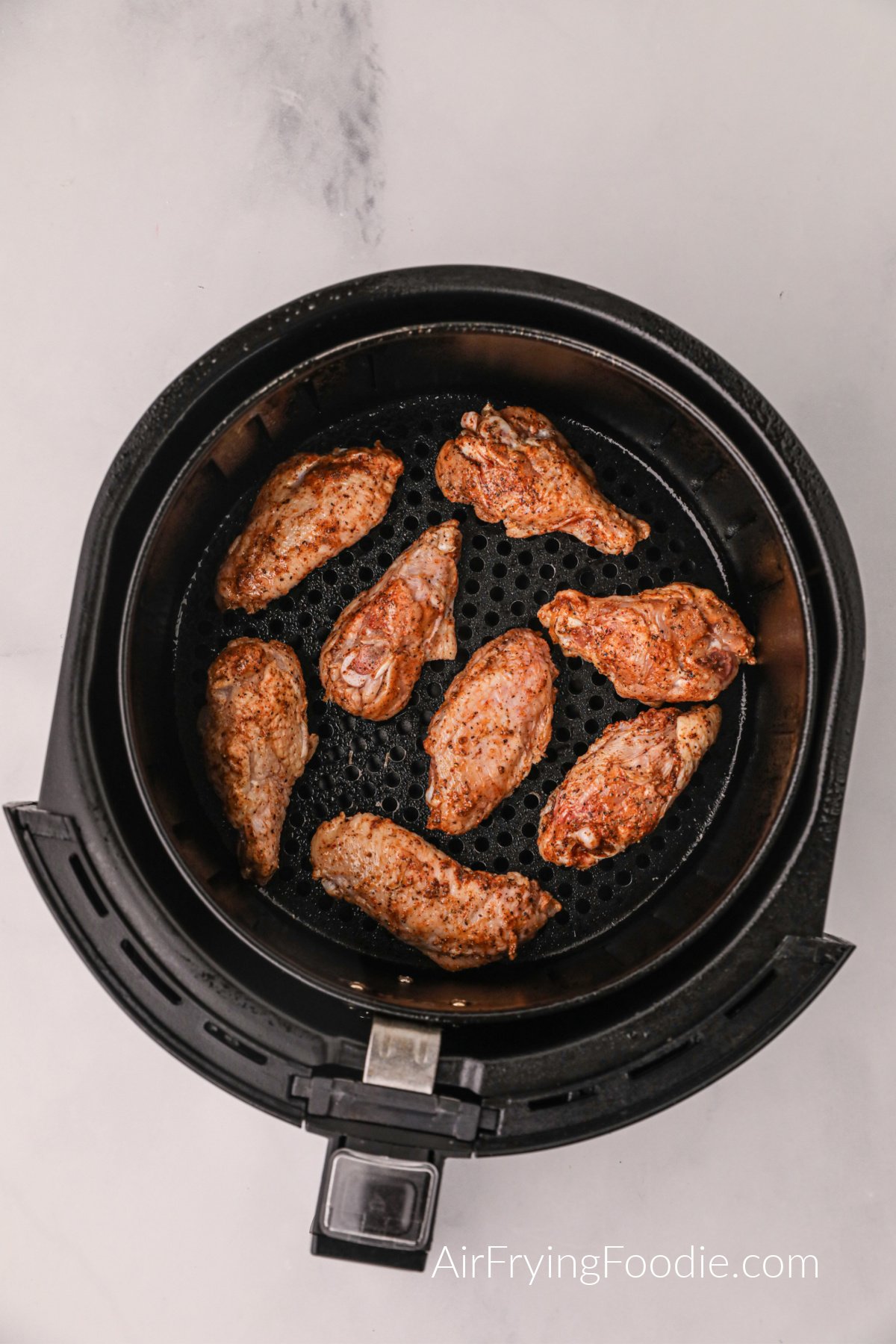 Seasoned chicken wings in the basket of the air fryer. 