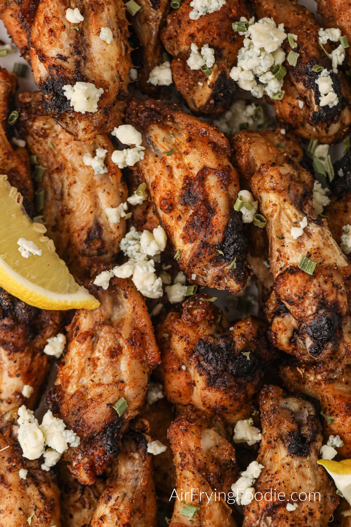 Closeup shot of air fryer lemon pepper wings with lemon wedges and blue cheese crumbles. 