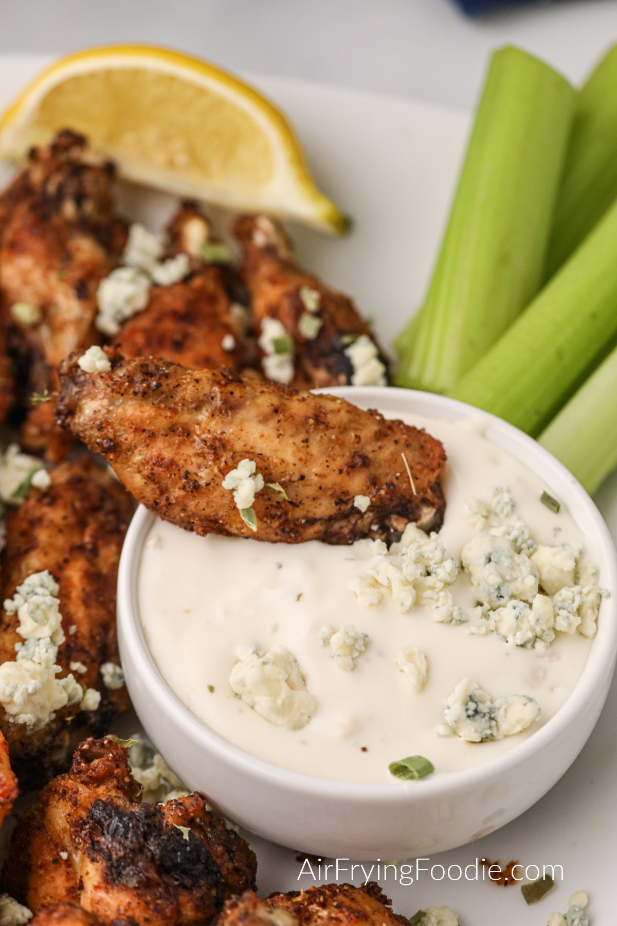 Lemon pepper wing being dipped into blue cheese dressing on a plate with a side of celery. 