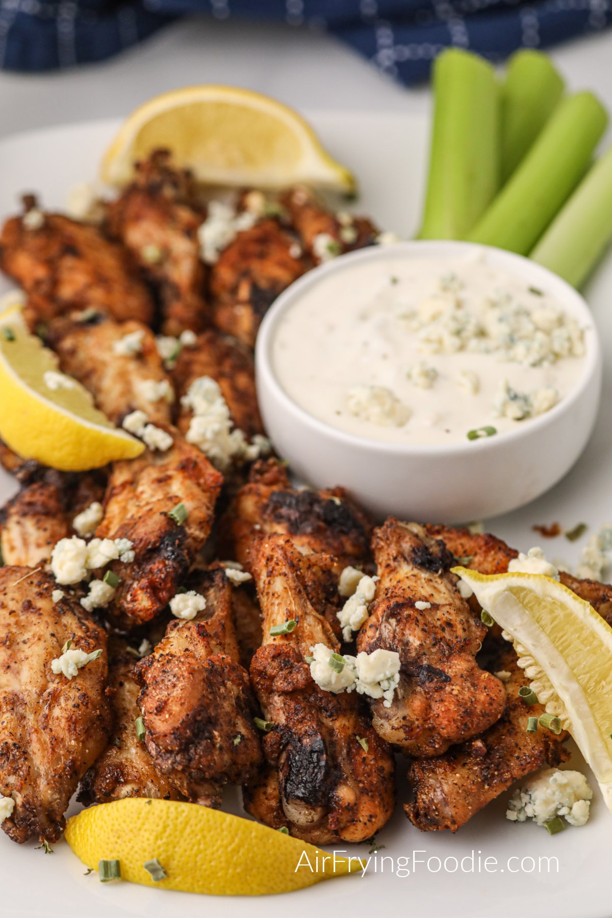Crispy Air Fryer Lemon Pepper Wings on a white serving plate with lemon wedges and blue cheese crumbles. 