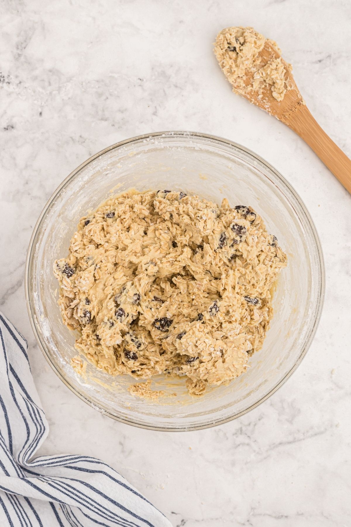 Oatmeal raisin cookie dough mixed in a clear glass bowl on a marble table. 