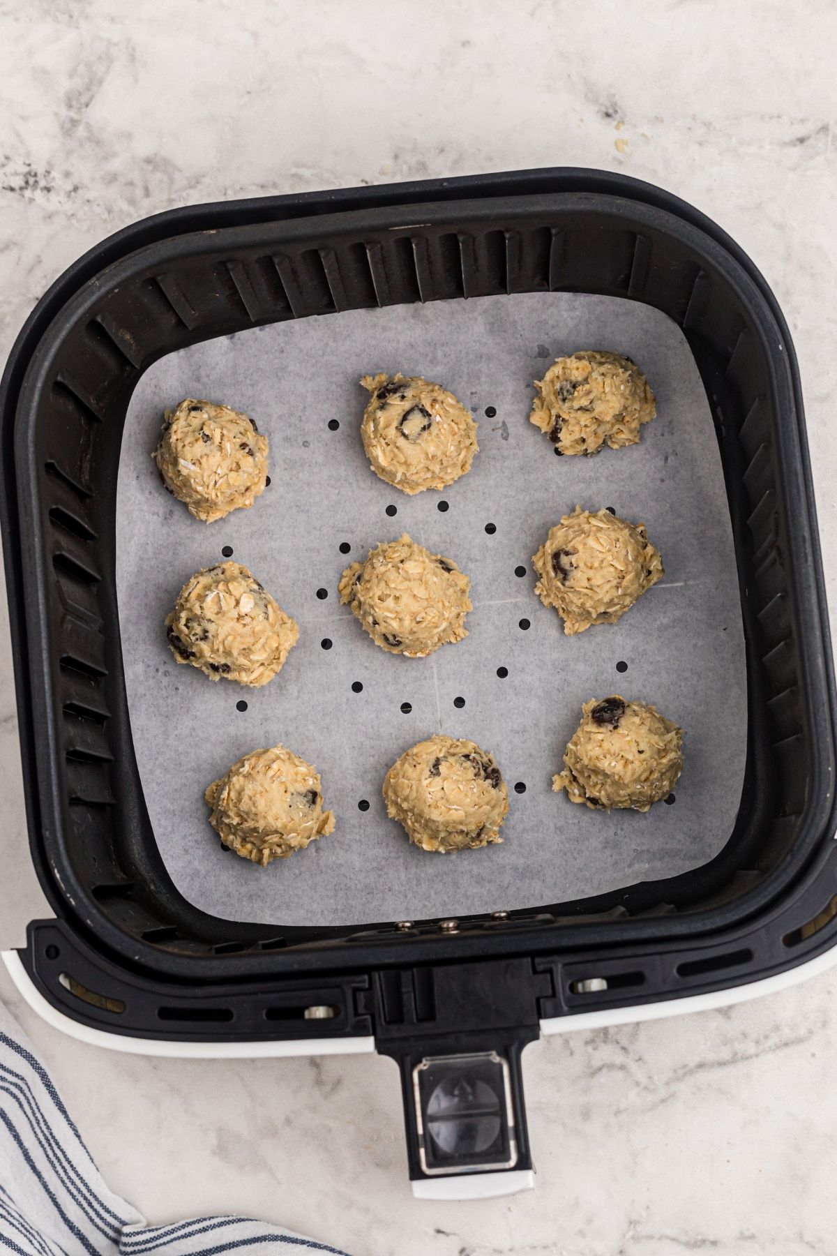 Cookie dough in balls placed in an air fryer basket lined with parchment paper