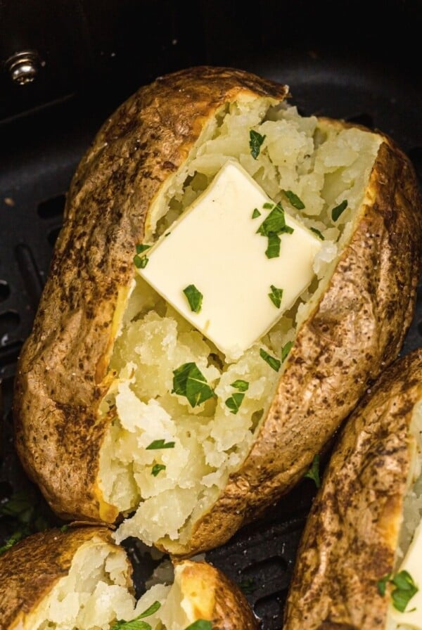 Golden baked potatoes in the air fryer basket after being cooked with butter and parsley flakes