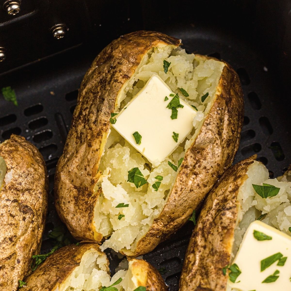 Golden baked potatoes in the air fryer basket after being cooked with butter and parsley flakes