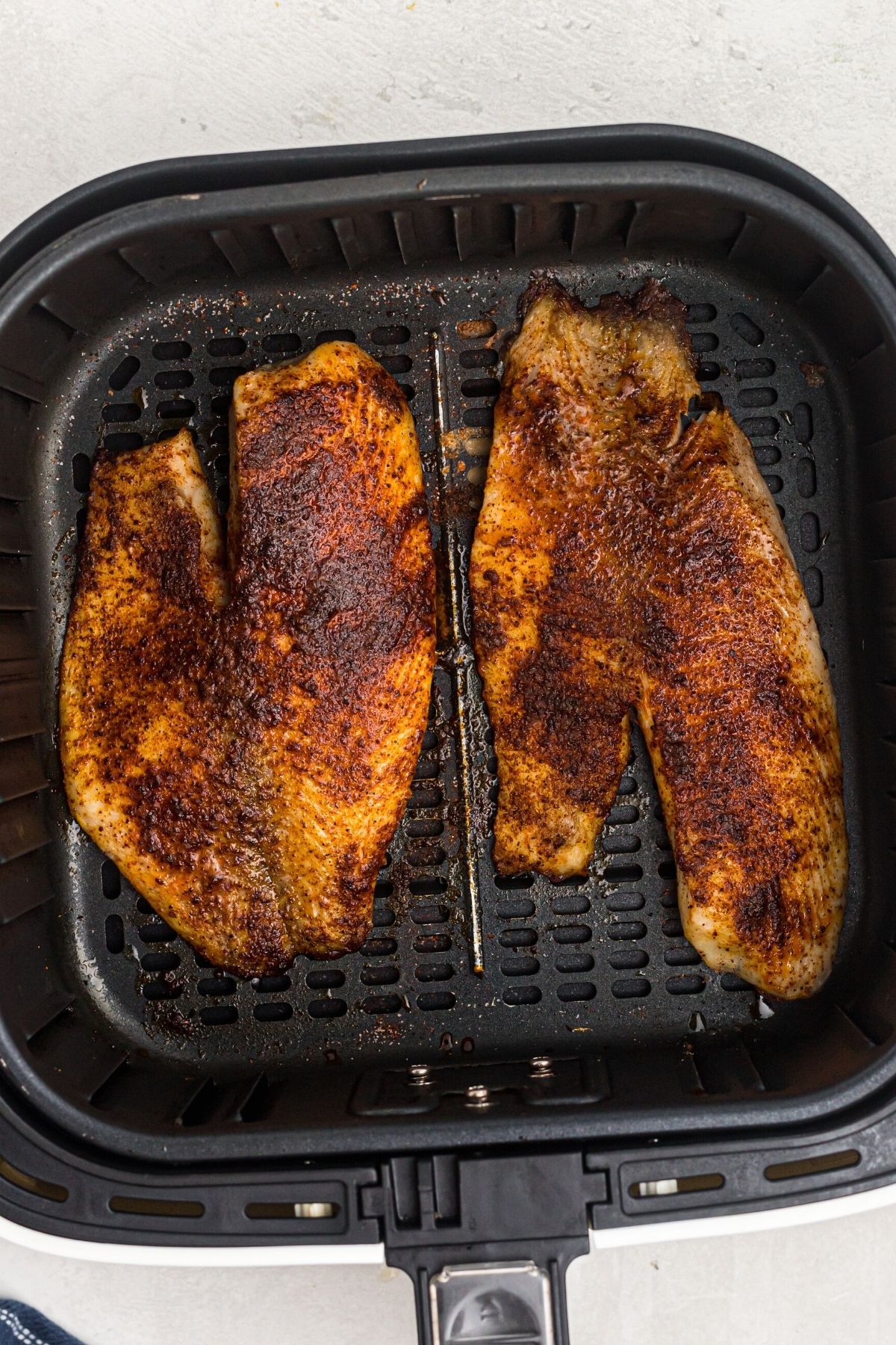 Golden brown cooked tilapia filets in the air fryer basket