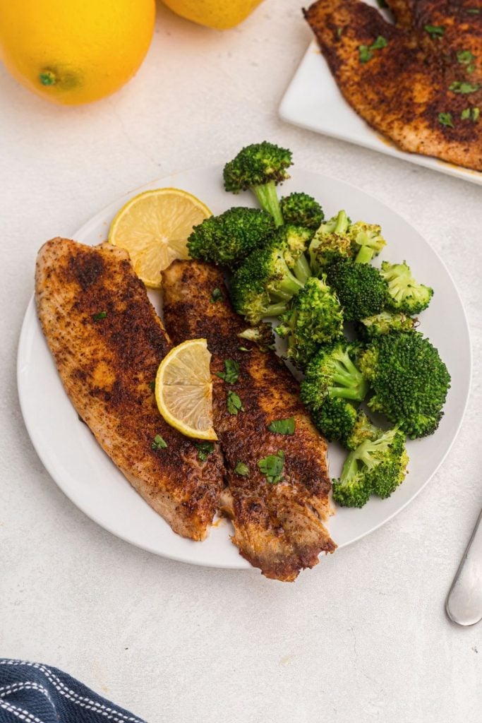 Golden seasoned tilapia cooked and served on a white plate with broccoli