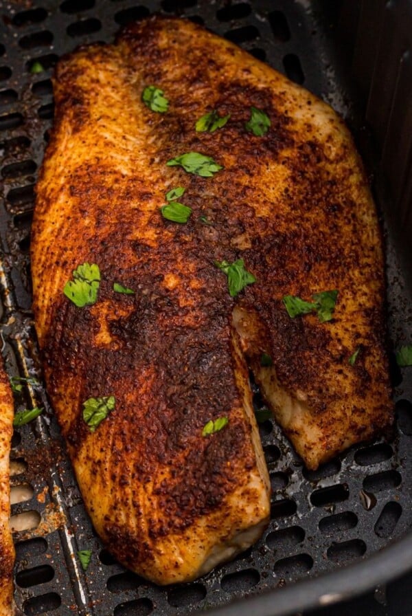 Golden brown cooked tilapia filets in the air fryer basket