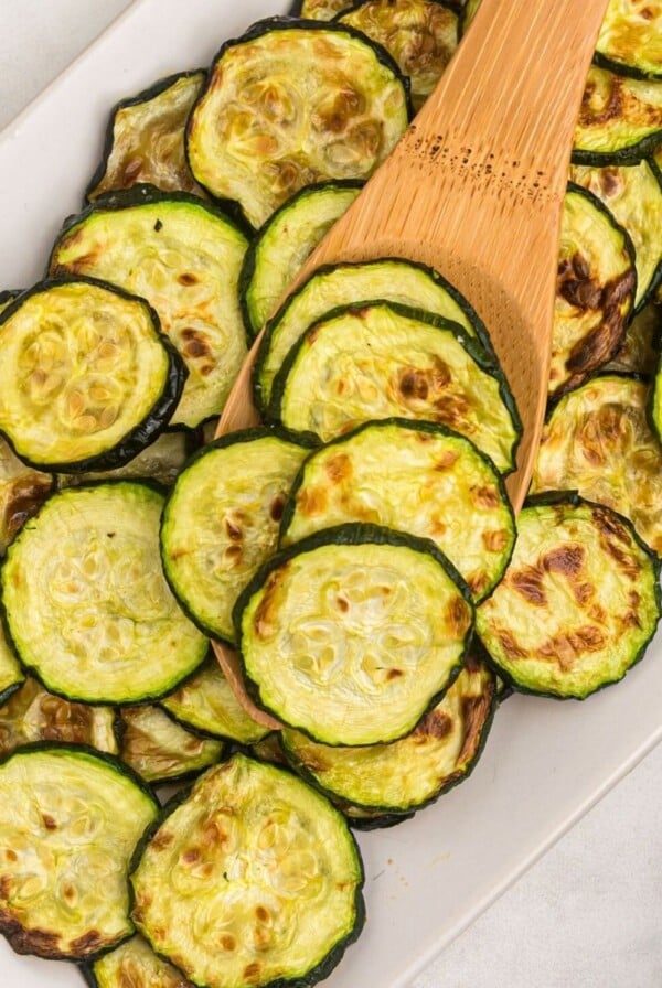 Golden cooked zucchini slices on a wooden spoon