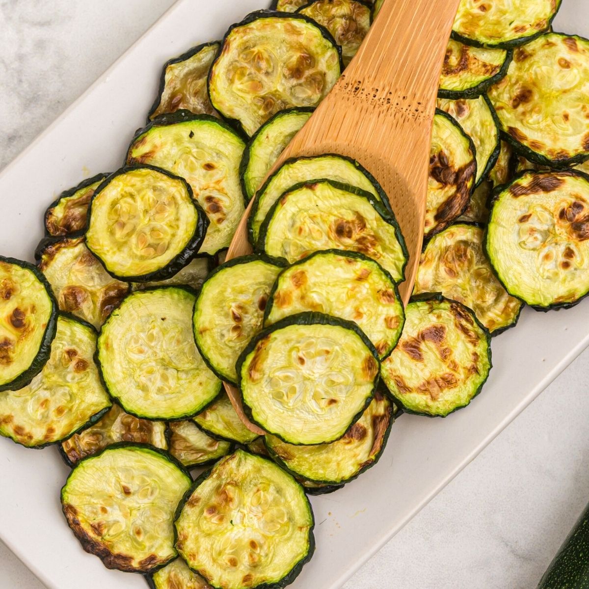 Golden cooked zucchini slices on a wooden spoon
