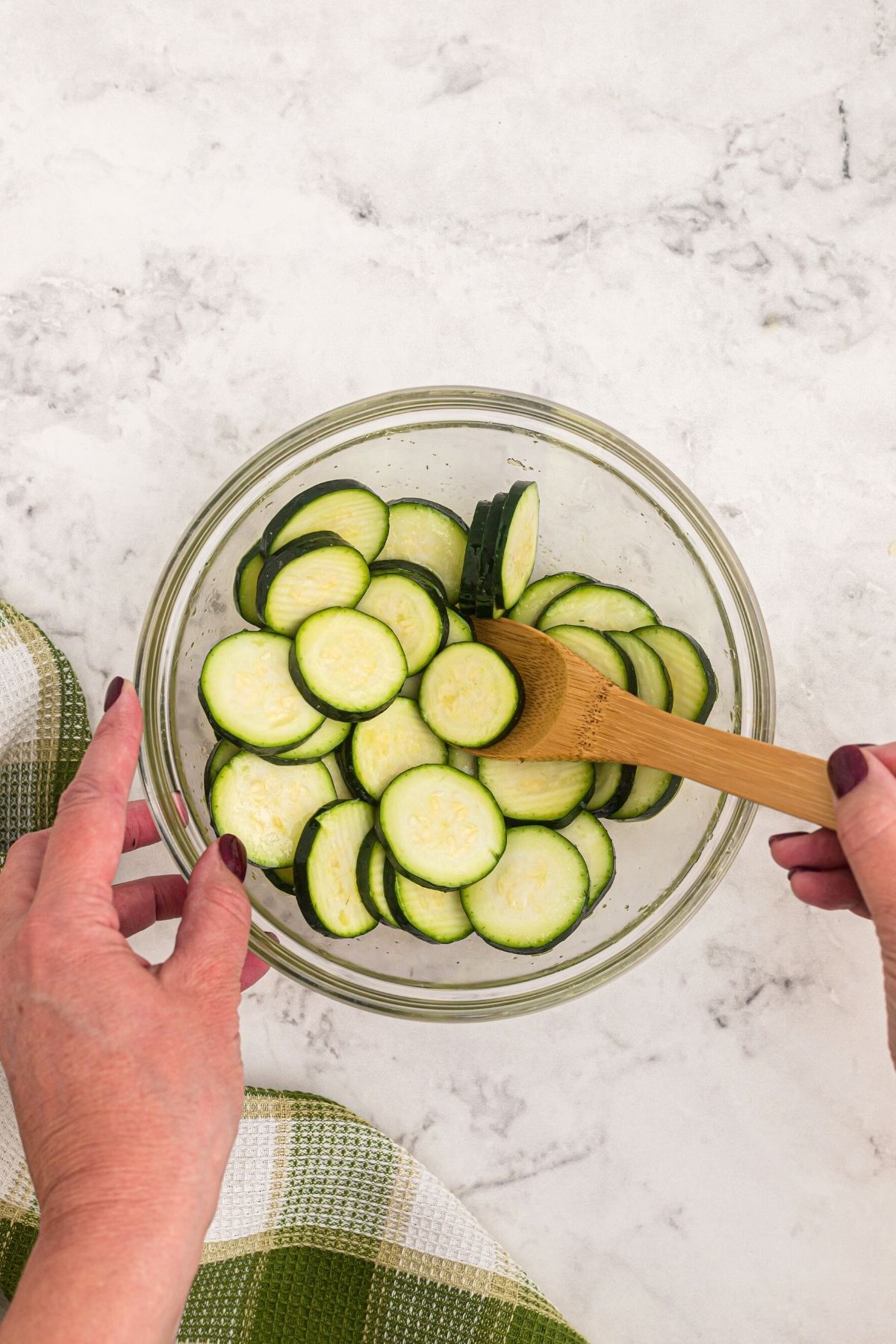glass bowl with slices of zucchini being tossed with olive oil and salt on a marble table