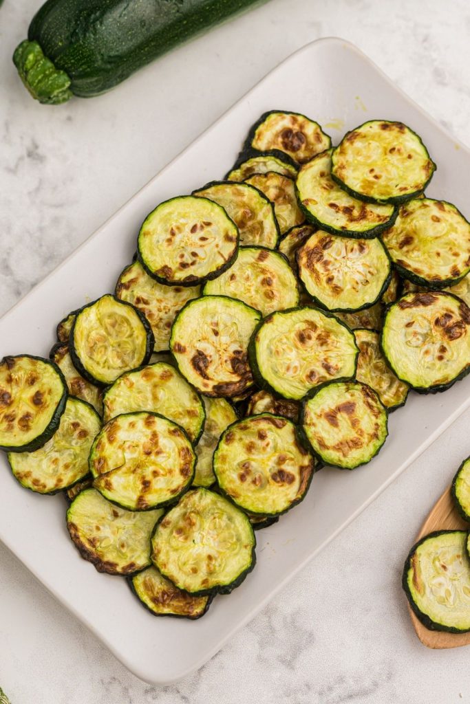 Golden cooked zucchini slices on a serving dish on a white marble table