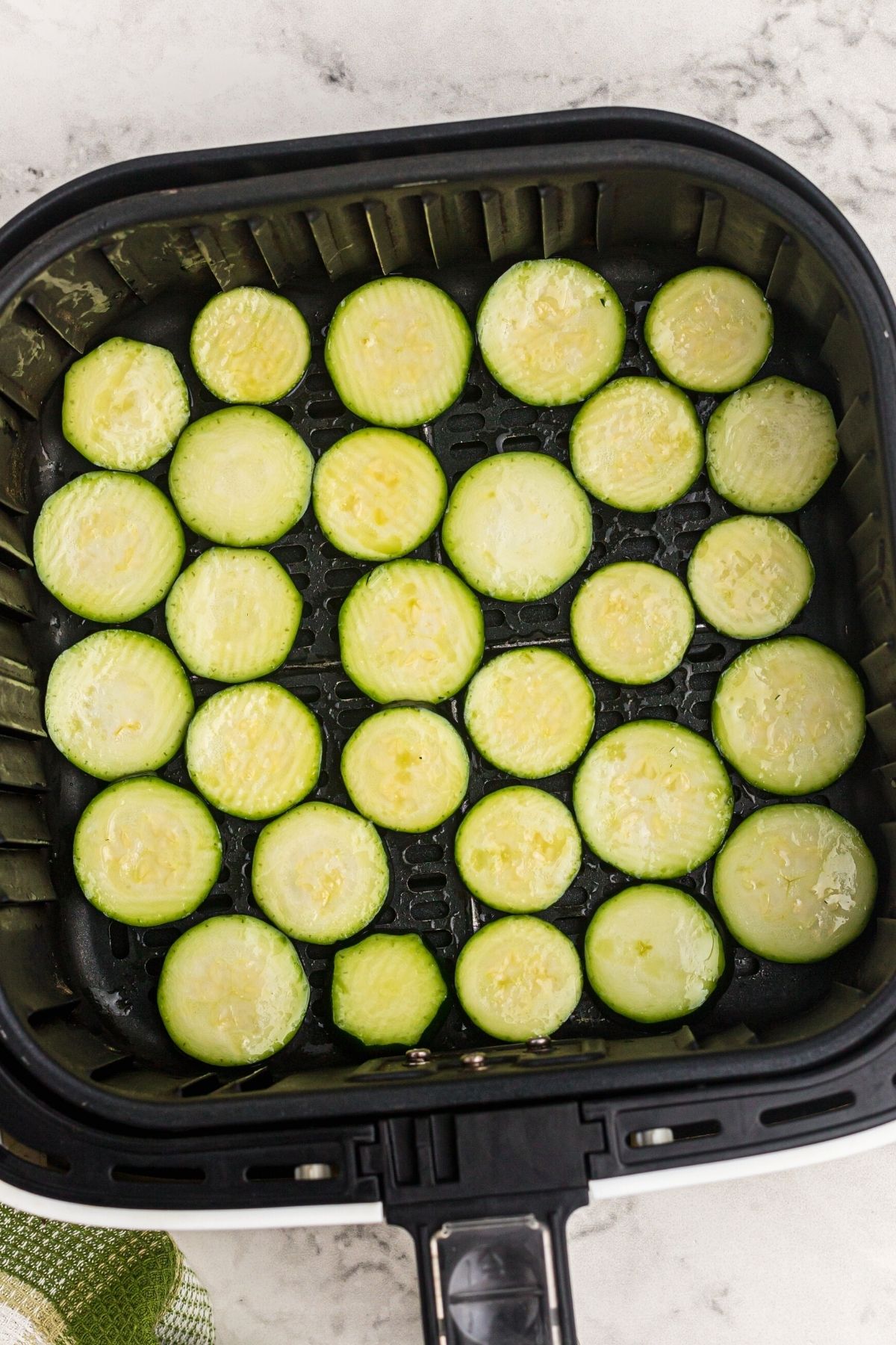 slices of zucchini in the air fryer basket after being tossed with olive oil and salt