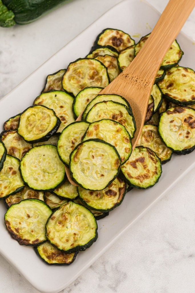 Wooden spoon scooping slices of cooked zucchini 