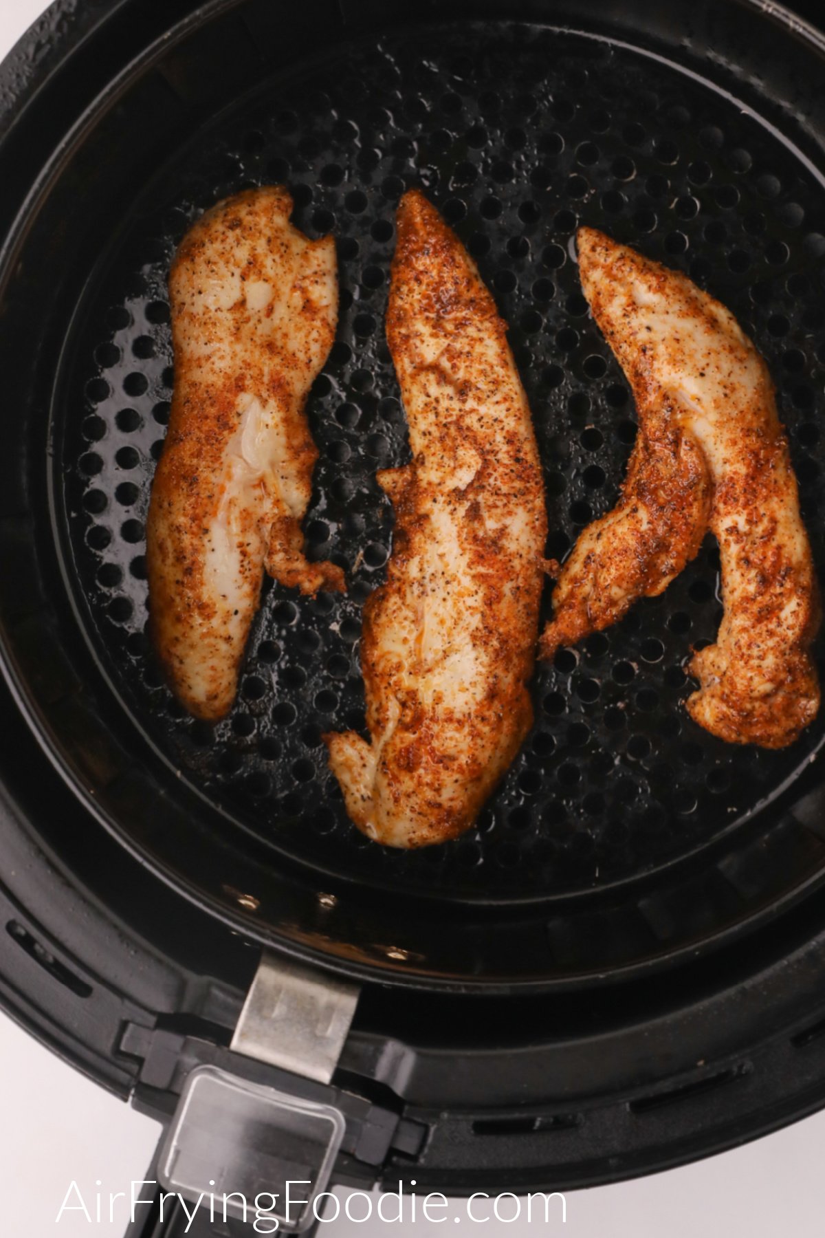 Cooked and seasoned naked chicken tenders in the air fryer basket, ready to serve.