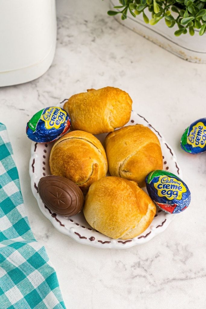 Four golden crescent wrapped eggs on a white plate with chocolate eggs on the table
