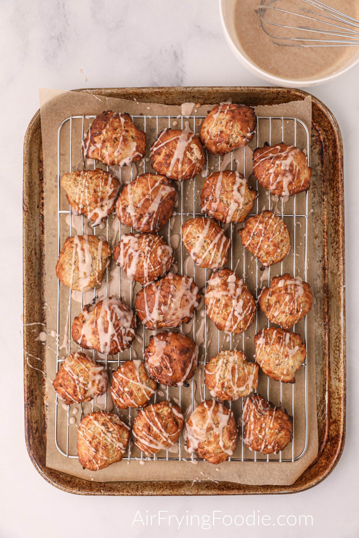 Apple fritters over a cooling rack with glaze drizzled over the top.