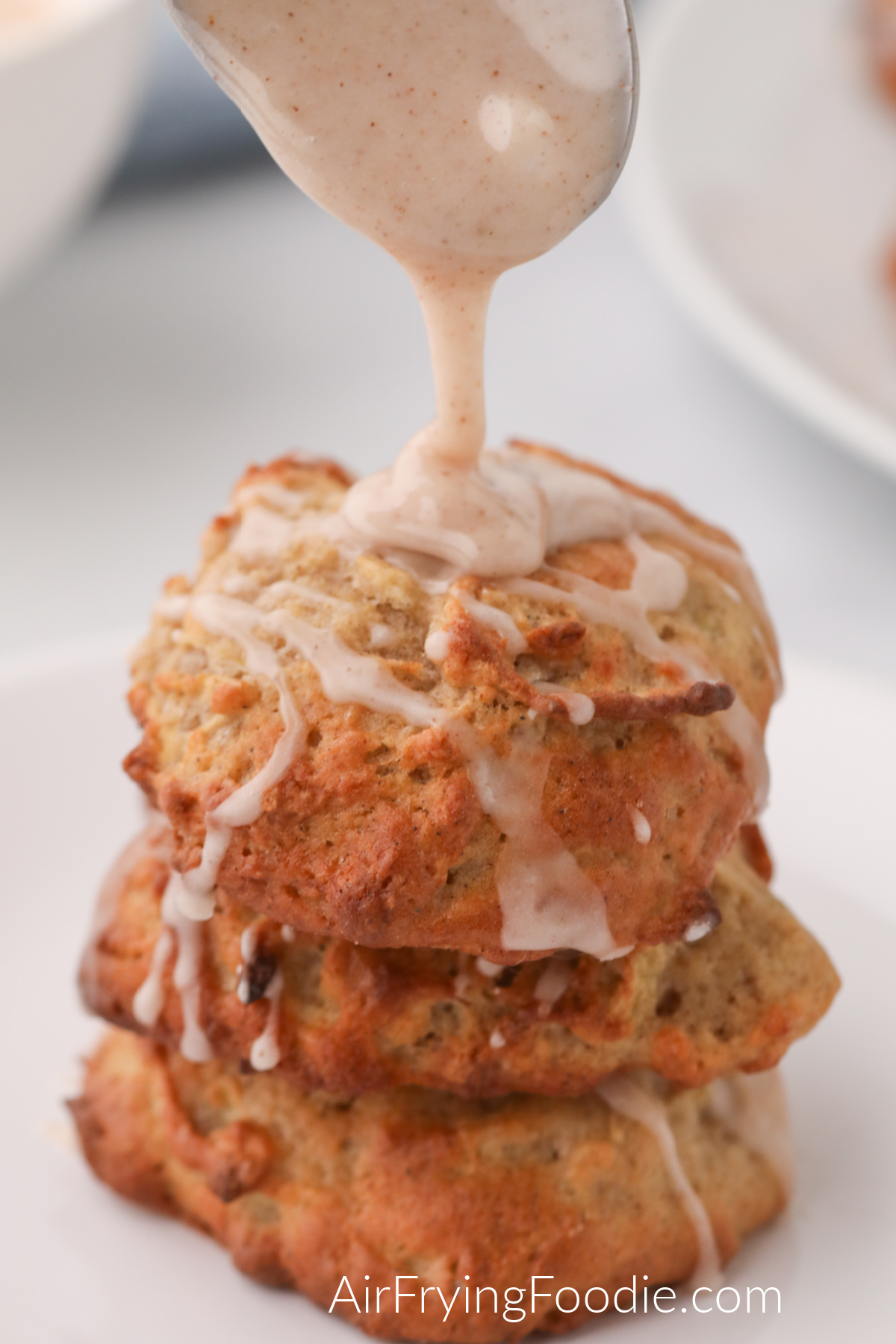Apple fritters stacked with a spoonful of glaze being drizzled over the top. 