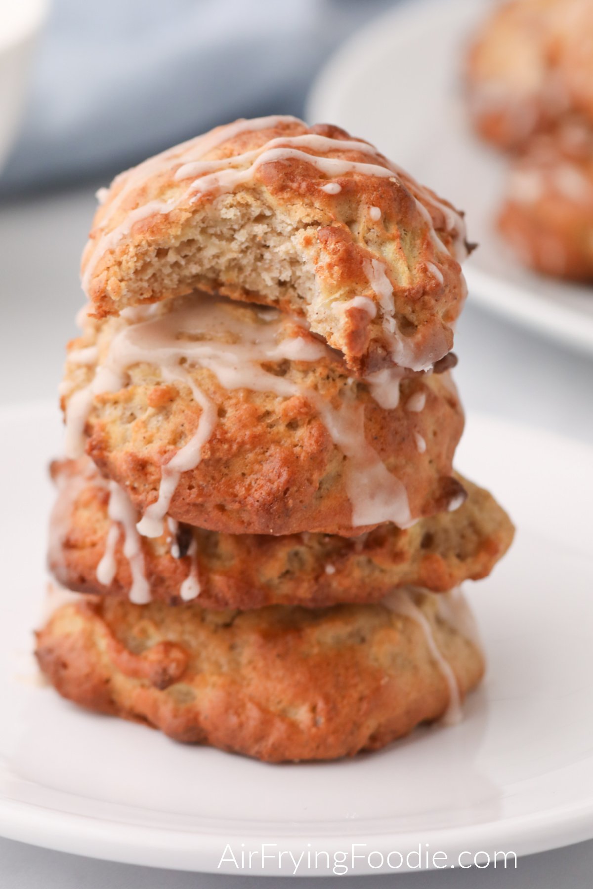 Apple fritters stacked on a plate, with the top fritter missing a bite. 