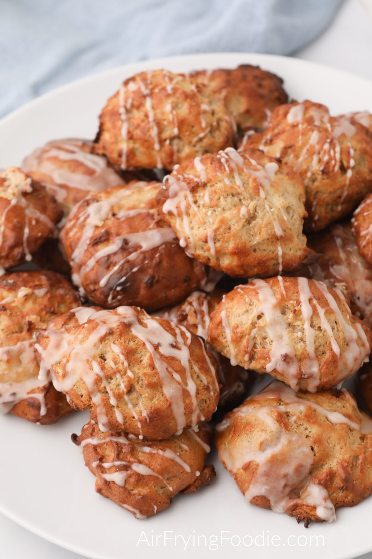 Apple fritters made in the air fryer and stacked on a white plate, covered in glaze, and ready to serve. 