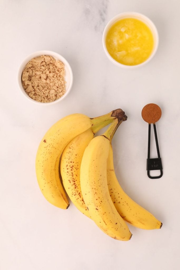 Ingredients needed to make air fryer bananas, measured and placed on a white marble table. 