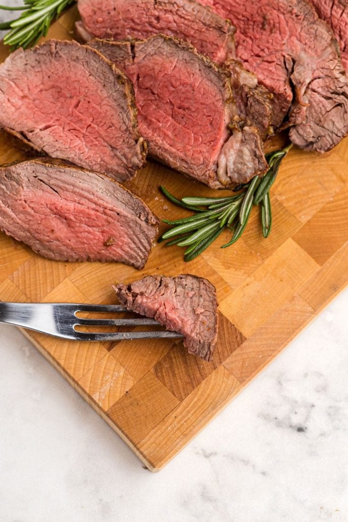 Juicy tenderloin on a cutting board with a piece on a serving fork.