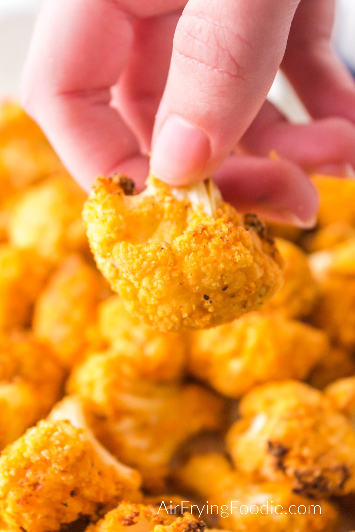 Air Fryer Buffalo Cauliflower on a white plate with a hand holding up a piece to eat. 