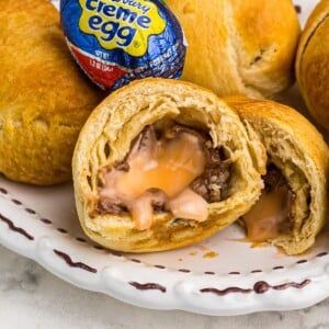 Golden crusted fried cadbury eggs with one cut open showing filling and stacked on a white plate.