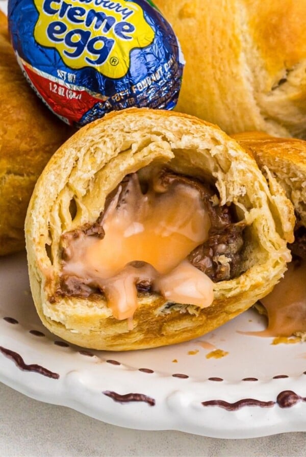 Golden crusted fried cadbury eggs with one cut open showing filling and stacked on a white plate.