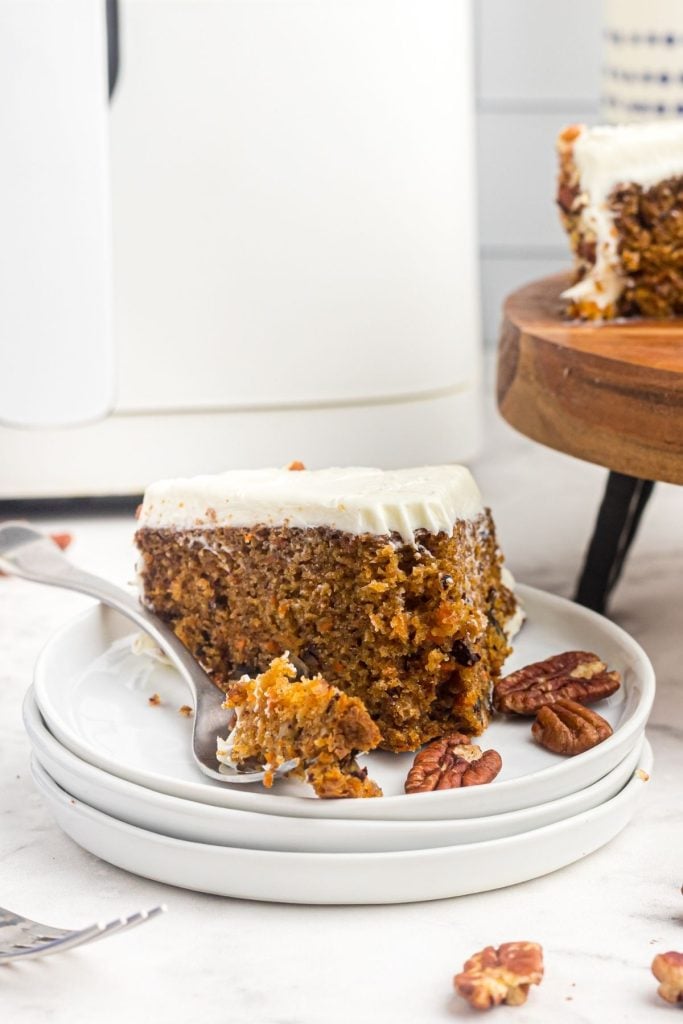 Slice of carrot cake with a bite on a fork and scattered pecans on the table