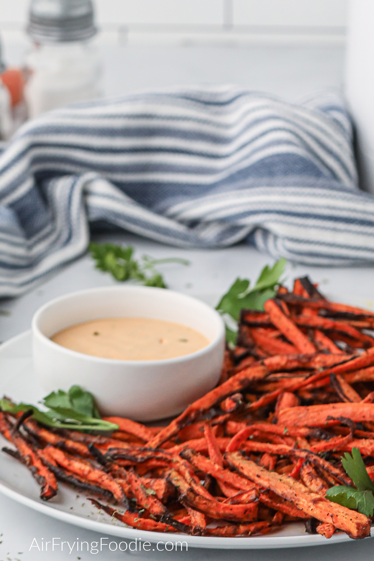 Air fryer carrot fries on a white plate with dipping sauce to serve. 