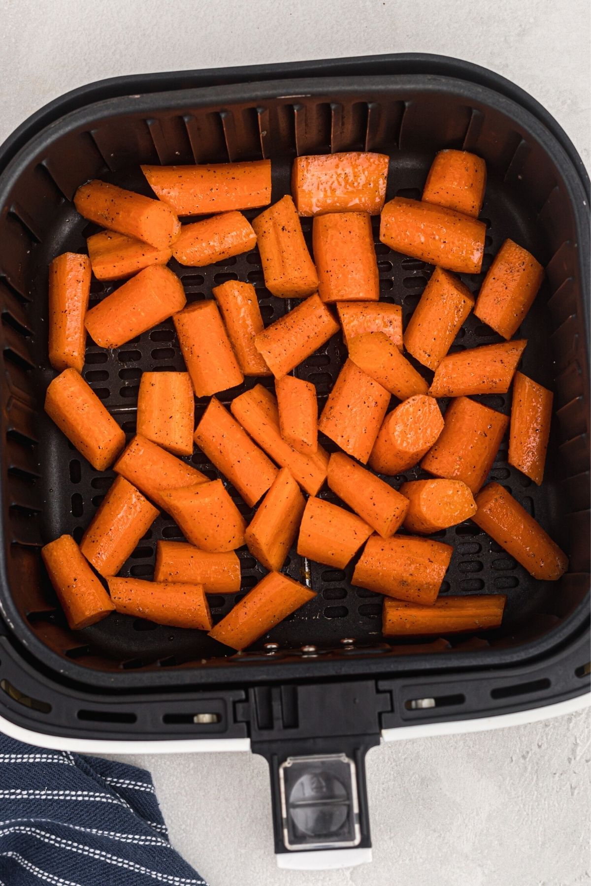 Uncooked chopped carrots in the air fryer basket after being seasoned