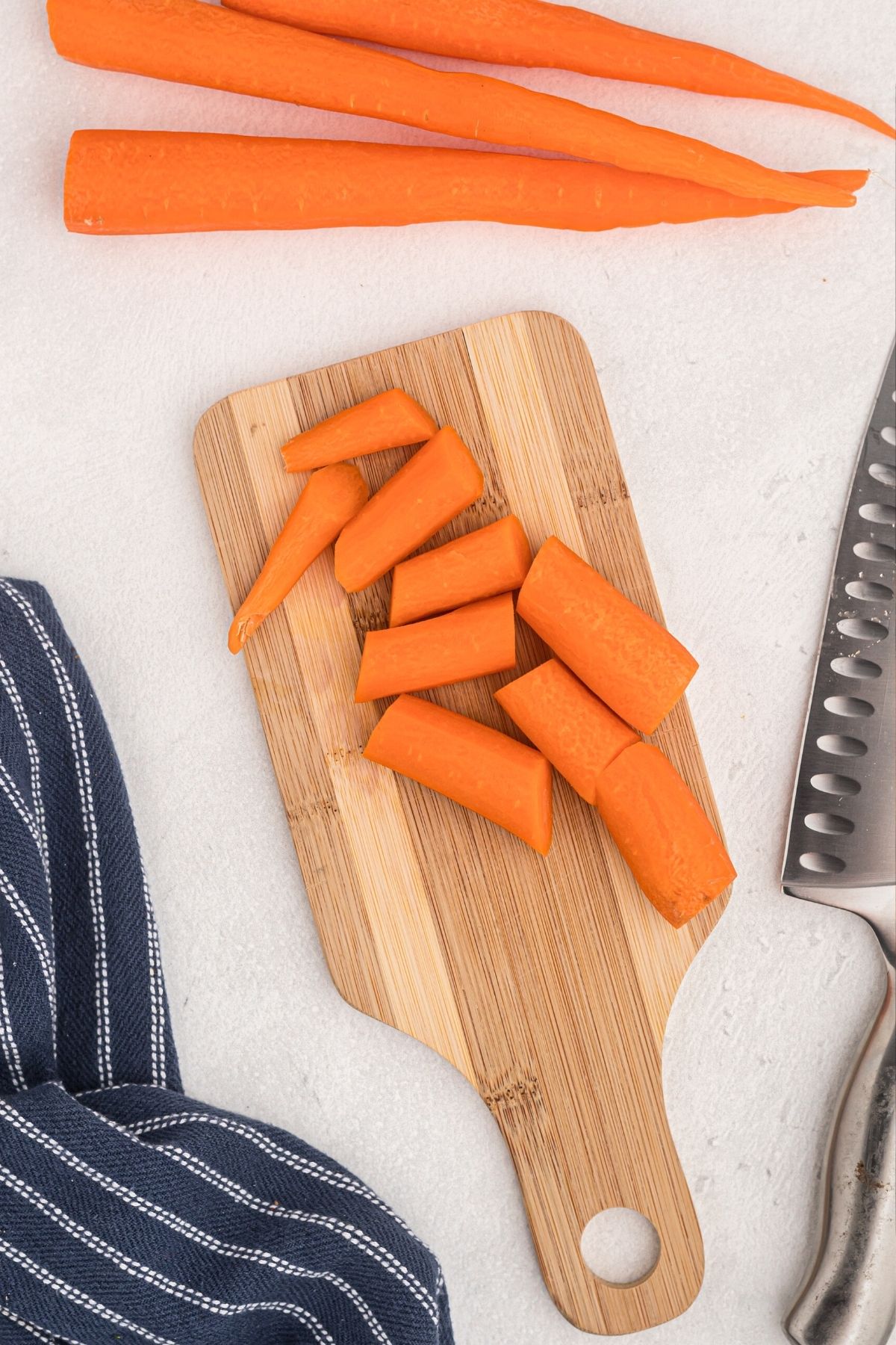 Carrots being sliced on a wooden cutting board with a knifr